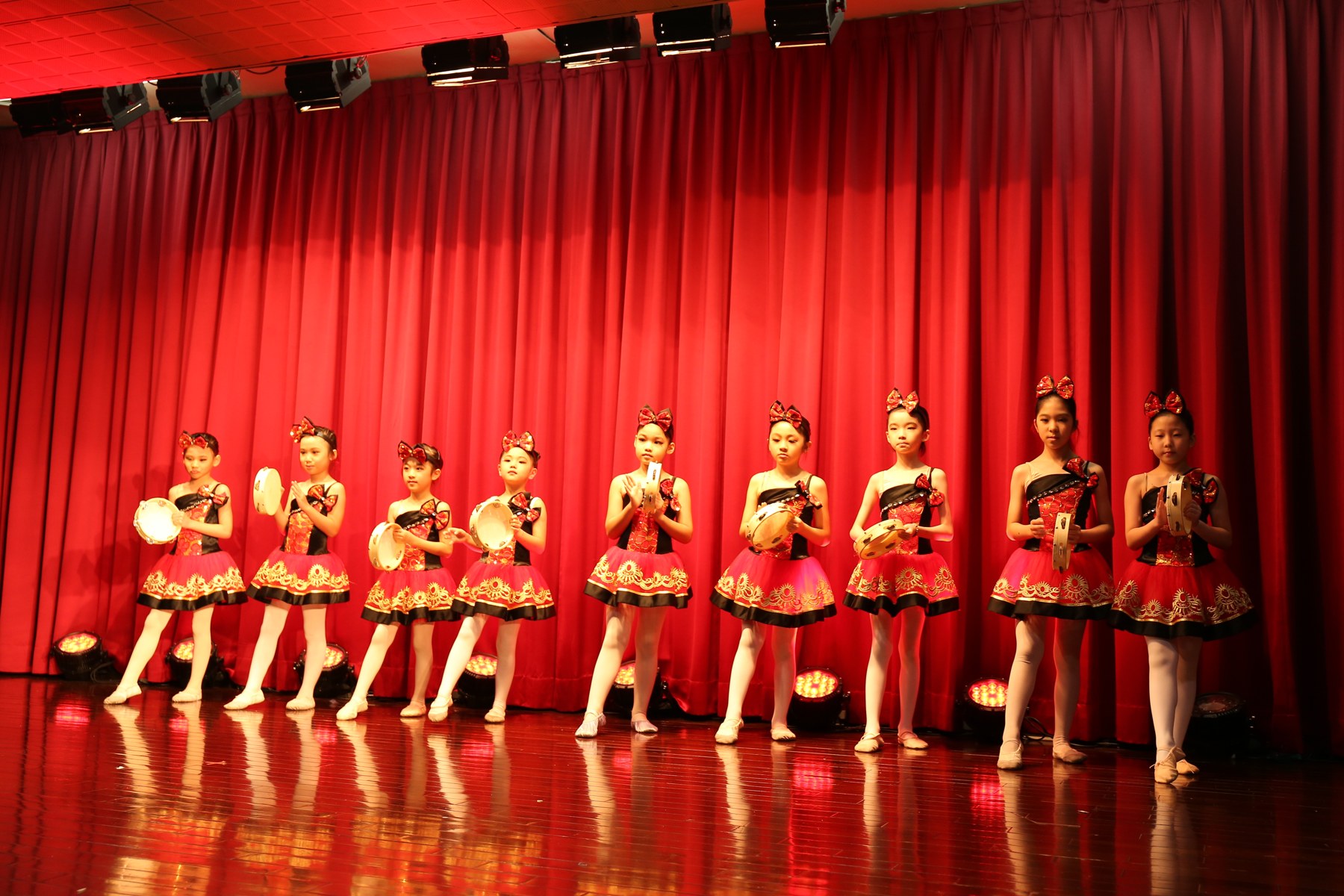 手持鈴鼓的舞者穿著紅黑色服裝排列演出